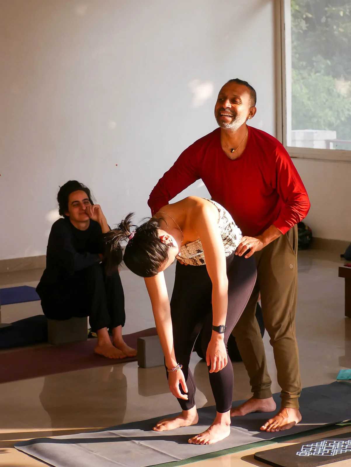 Parveen Nair steadying a student in a backbend, both of them laughing