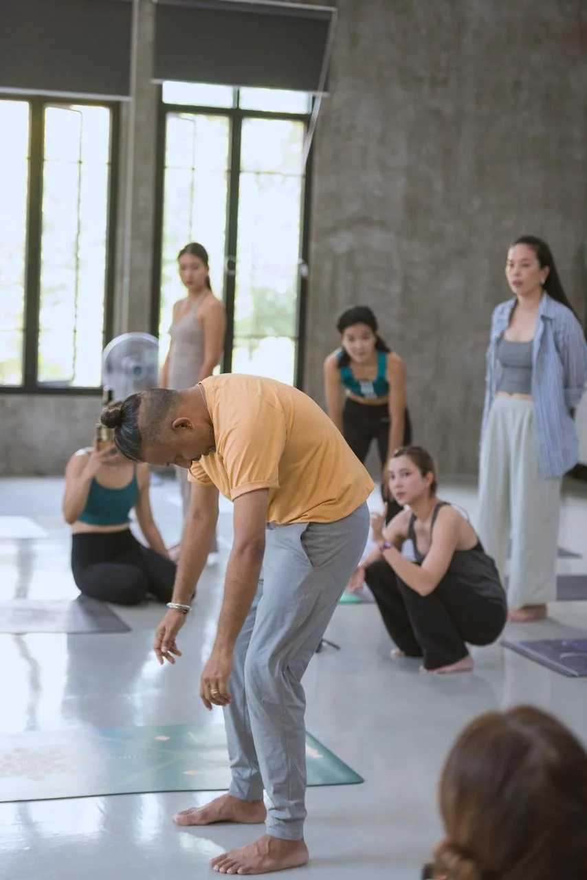 Parveen Nair guiding a forward fold while the class looks on