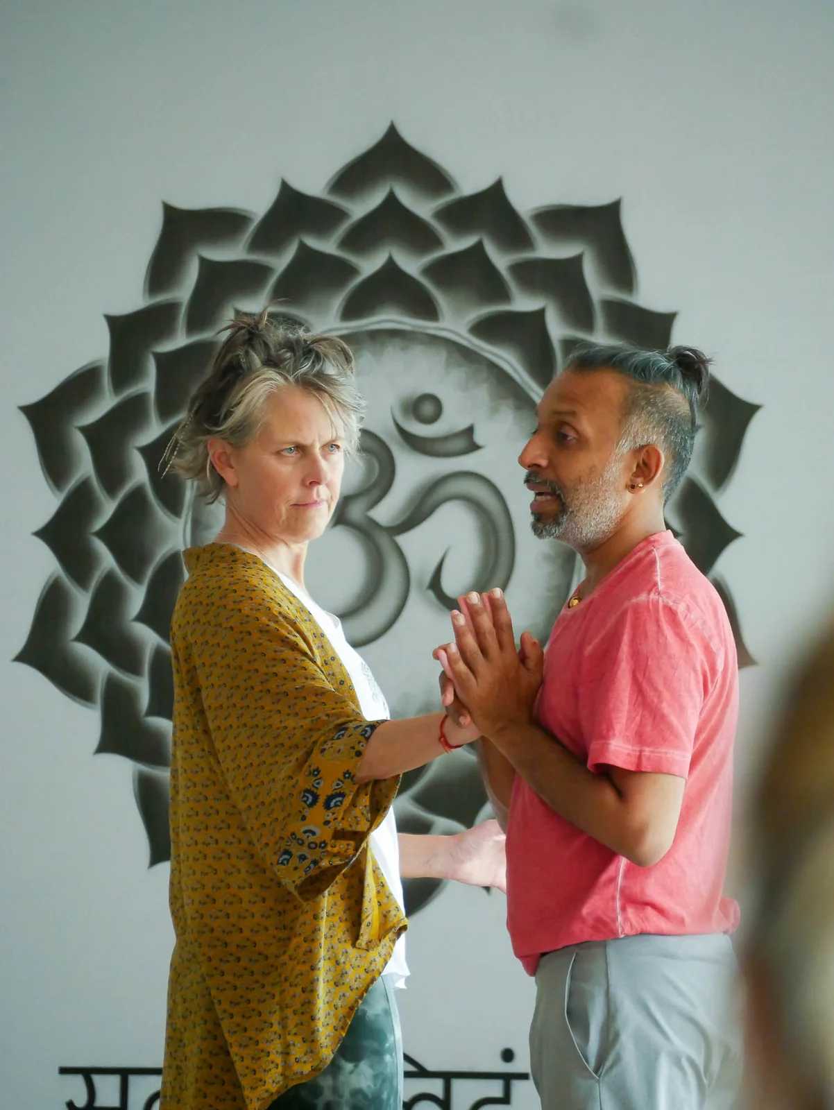 Parveen Nair and a student greeting each other in front of a painted mandala