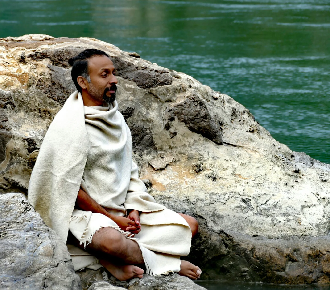 Parveen Nair seated in a shawl on the rocks beside the Ganga
